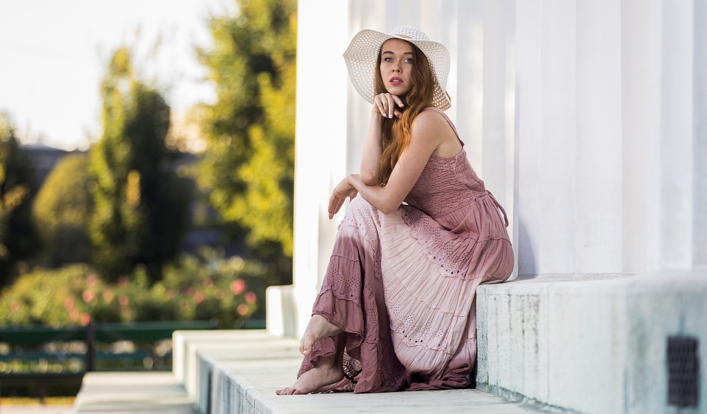 Красивая девушка в белой шляпе сидит на ступеньках 
