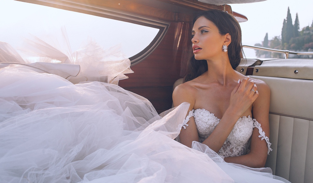 Красивая девушка в белом свадебном платье в машине