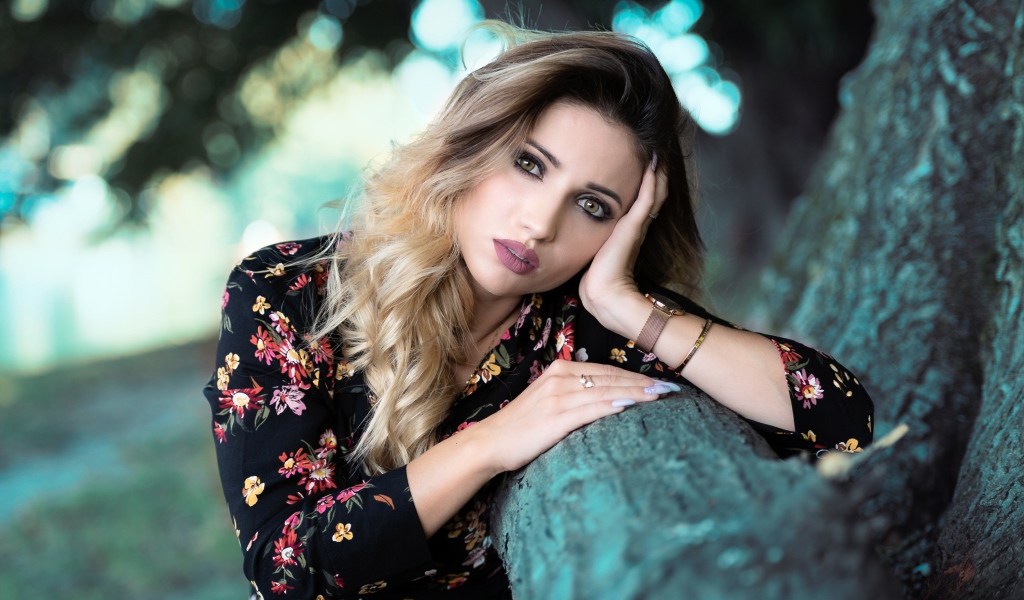 Красивая девушка в цветастом платье у дерева