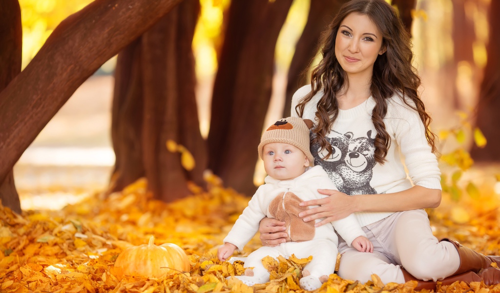 Красивая девушка сидит с грудным ребенком на опавшей листве