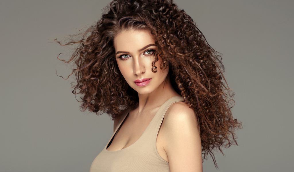 Красивая девушка с накрученными волосами на сером фоне