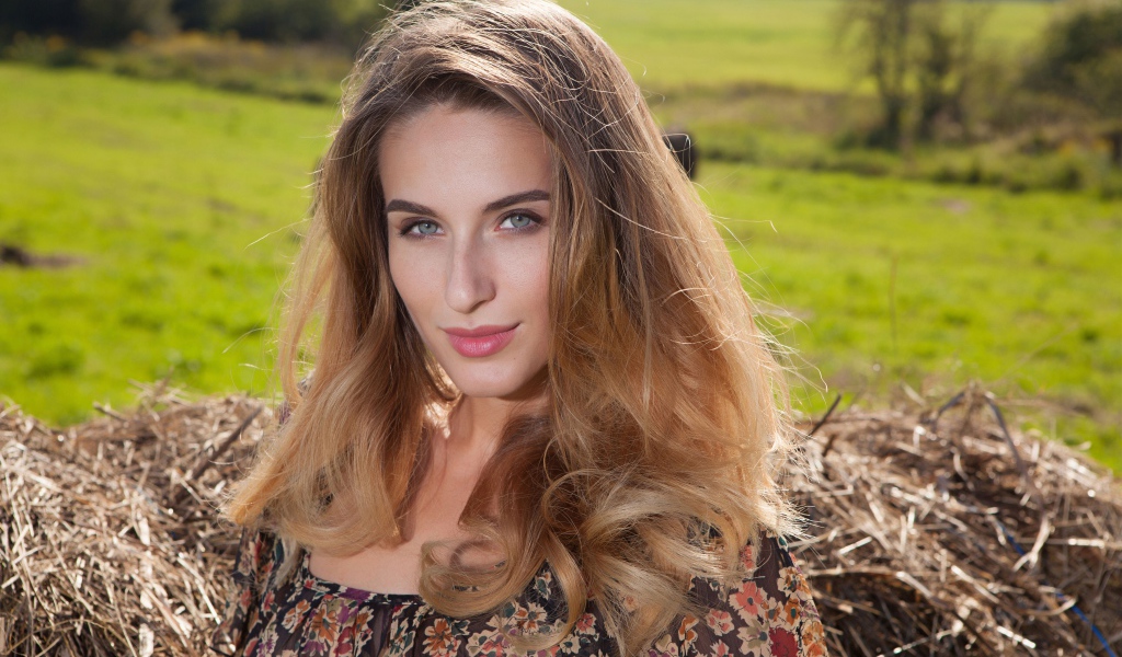 Красивая девушка с серыми глазами стоит у сена