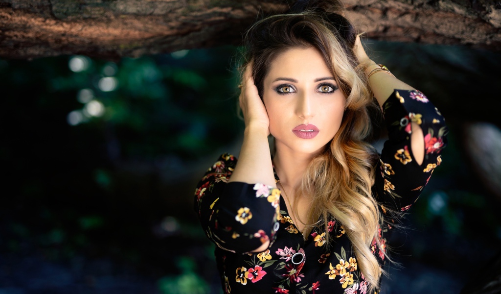 Красивая девушка с руками в волосах у дерева