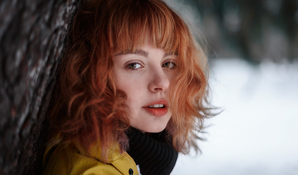 Красивая рыжеволосая девушка стоит у дерева зимой