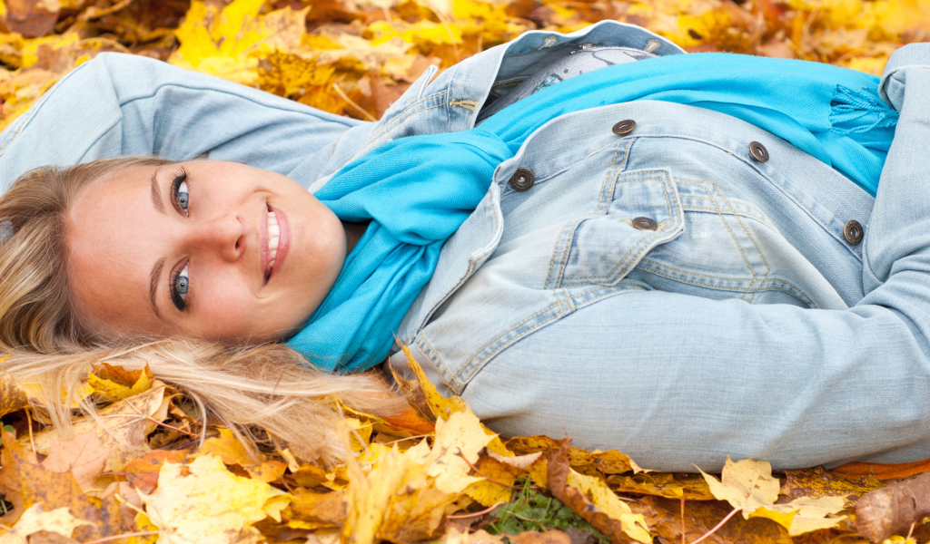 Красивая улыбающаяся девушка лежит на желтых листьях 