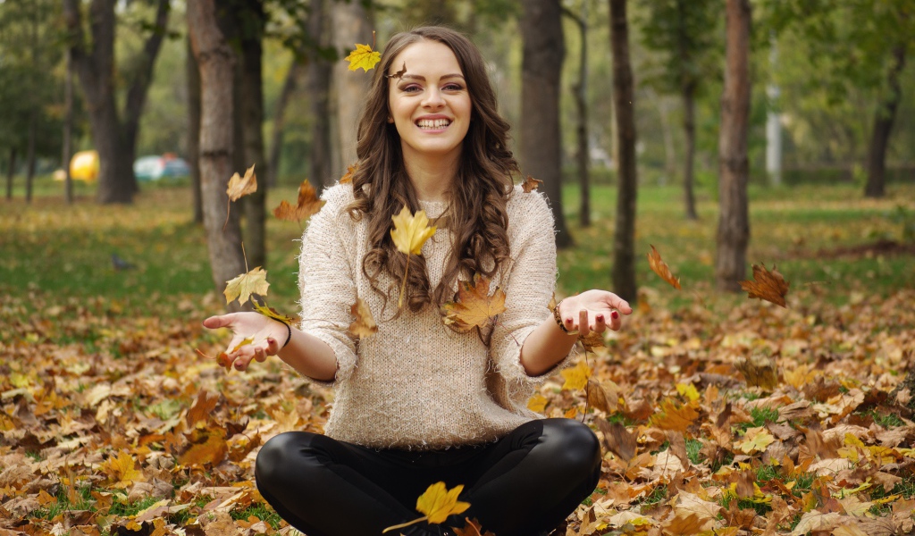 Красивая улыбающаяся девушка сидит на земле с желтыми листьями