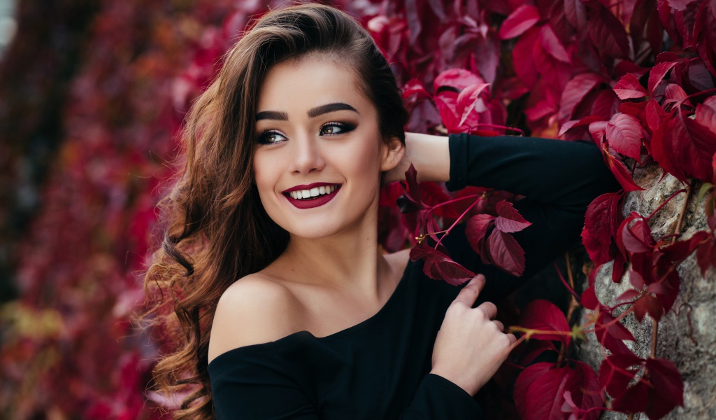 Красивая улыбающаяся длинноволосая девушка у стены с декоративным виноградом