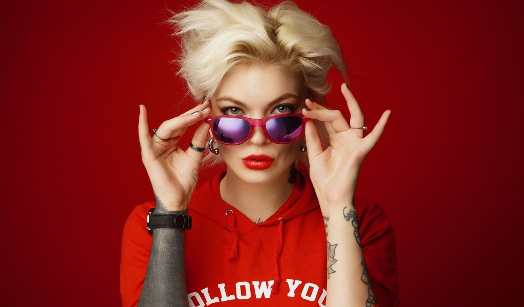 Яркая блондинка с татуировками на руках на красном фоне