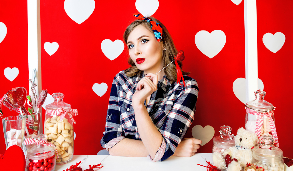 Яркая девушка за столом со сладостями на красном фоне с белыми сердечками 