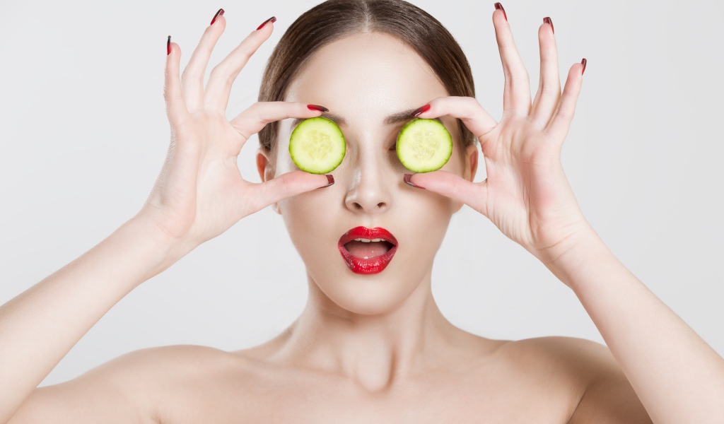 Яркая девушка с огурцами у глаз на сером фоне