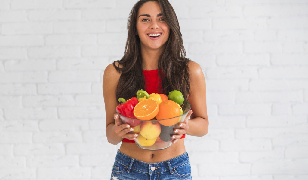 Брюнетка с миской фруктов на фоне стены