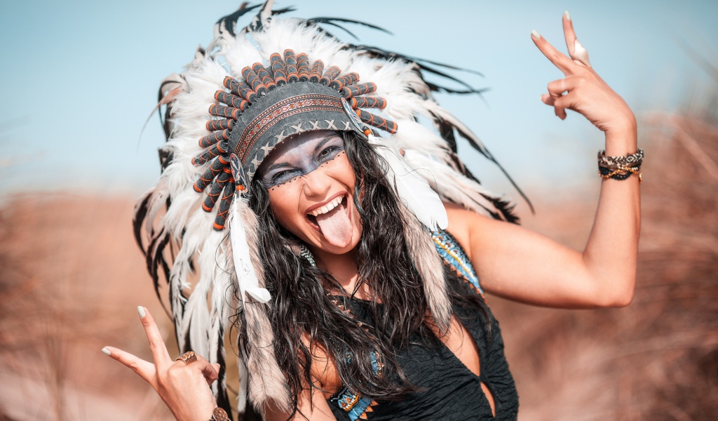 Веселая девушка с высунутым языком в костюме индейца