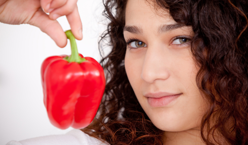Лицо девушки с красным сладким перцем в руке крупным планом