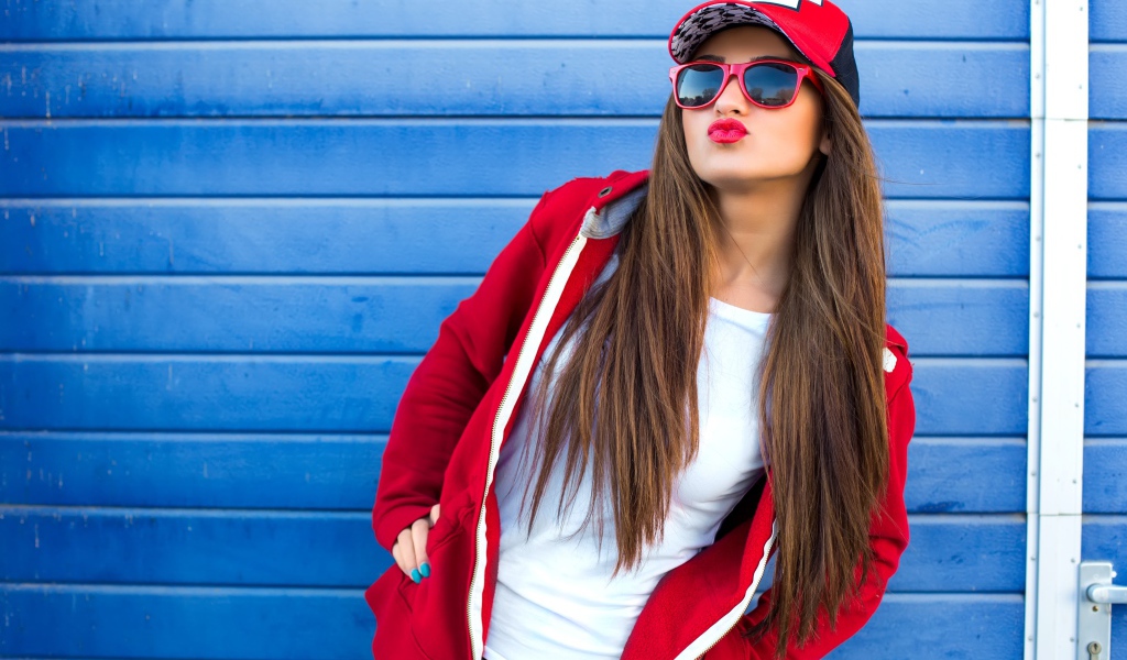 Девушка в бейсболке и солнечных очках у стены