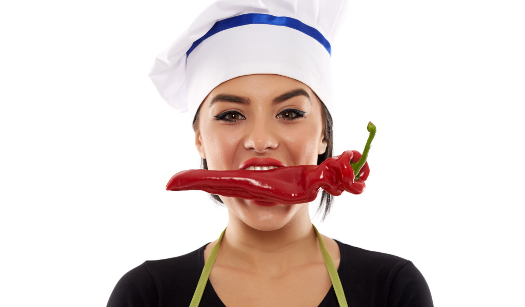 Девушка в шапке повара с красным перцем во рту на белом фоне