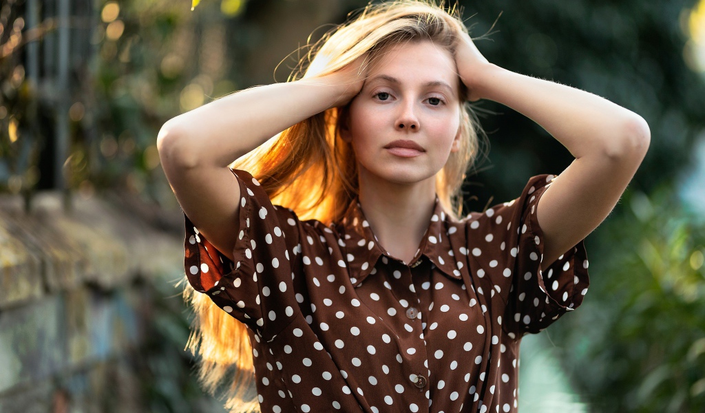 Девушка в рубашке в горох с руками в волосах 