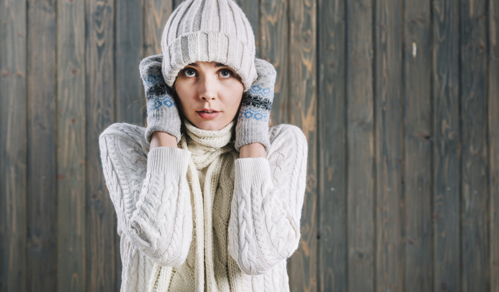 Девушка в варежках поправляет шапку на голове