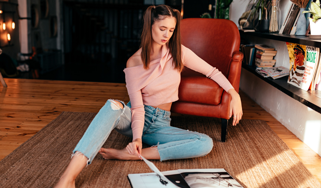 Девушка читает журнал на полу у кожаного кресла