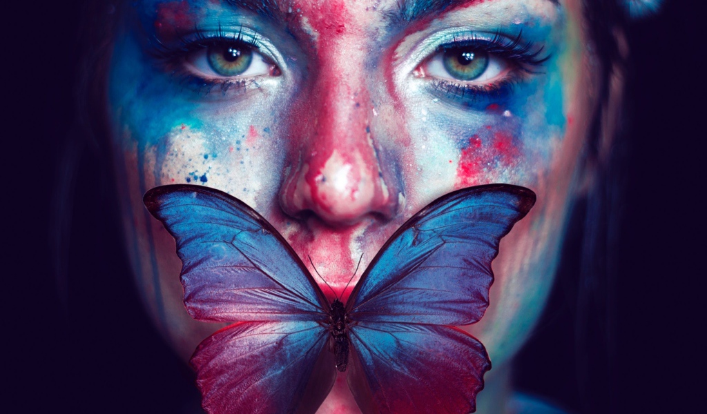 Лицо девушки в краске с бабочкой во рту