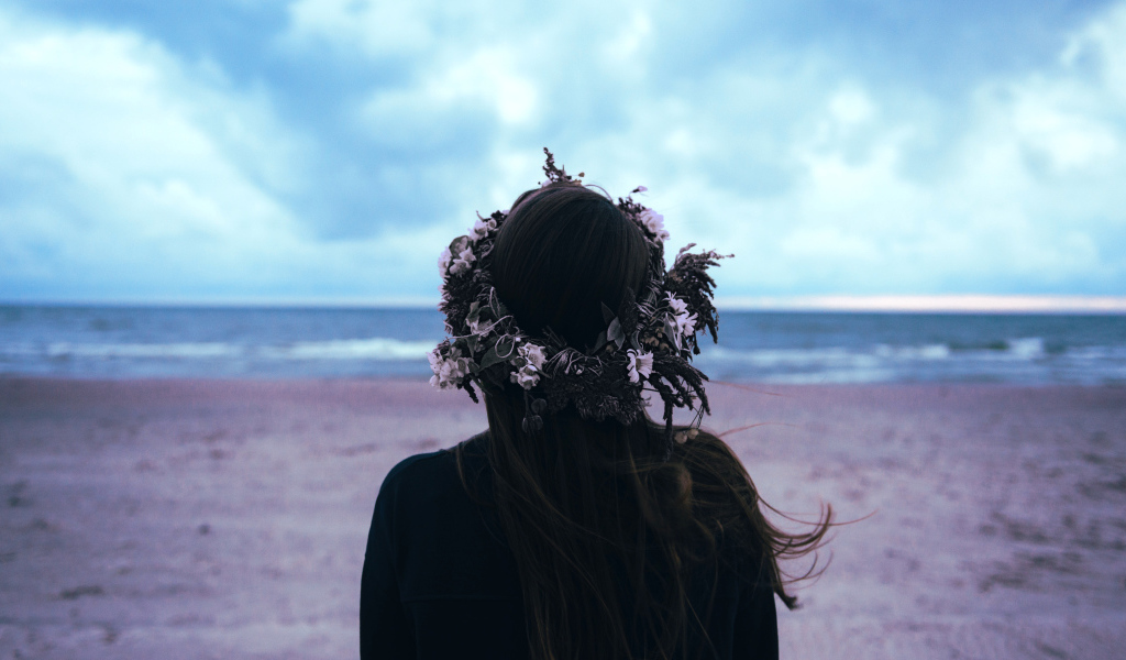 Девушка с венком на голове на фоне моря вид сзади