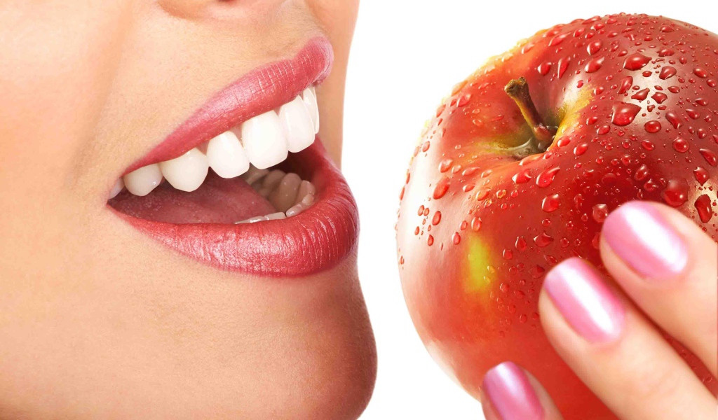 Девушка с красивыми белыми зубами кусает яблоко