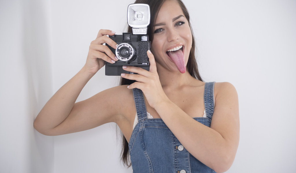 Девушка с высунутым языком с фотоаппаратом в руках