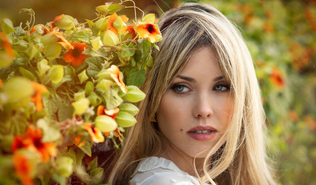 Зеленоглазая блондинка у забора с цветами 