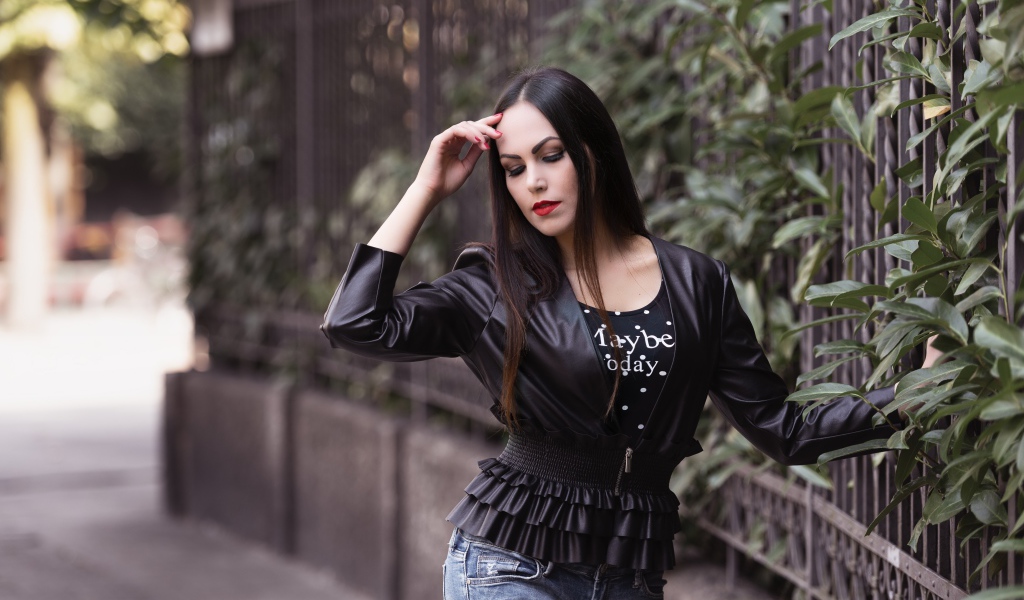 Длинноволосая брюнетка в черной куртке у забора