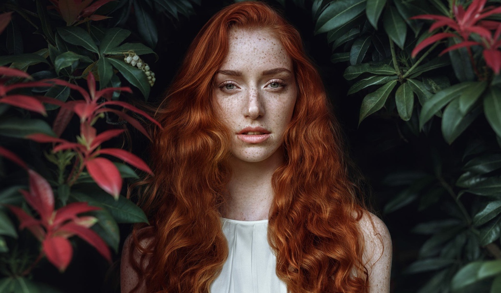 Рыжеволосая девушка с веснушками на лице на фоне кустов 