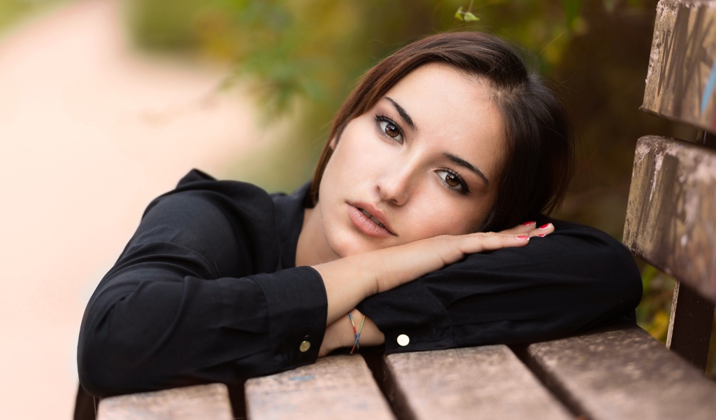 Грустная кареглазая девушка лежит на деревянной лавке