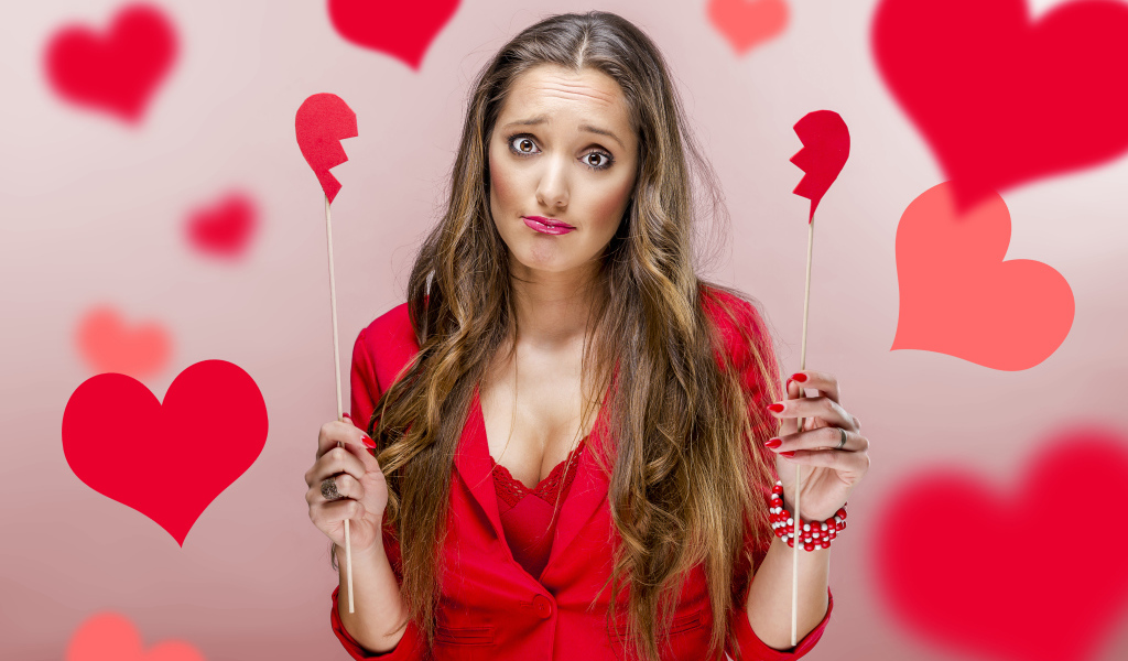 Грустная девушка с половинками бумажного сердца в руках 