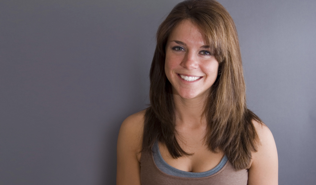 Улыбающаяся милая девушка у серой стены