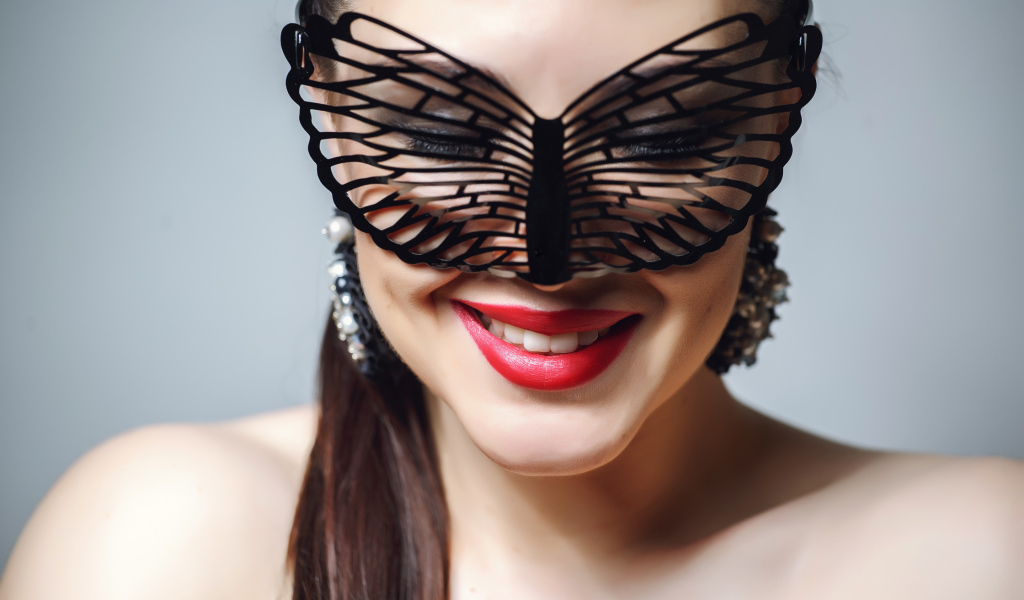 Улыбающаяся девушка в черной маске на сером фоне