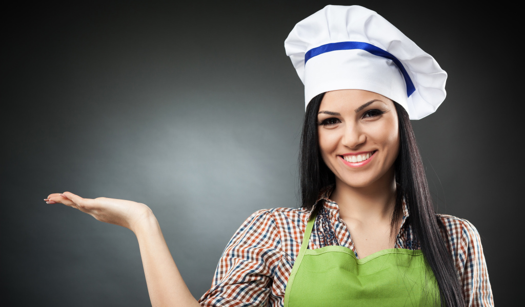 Улыбающаяся девушка в поварском колпаке на сером фоне