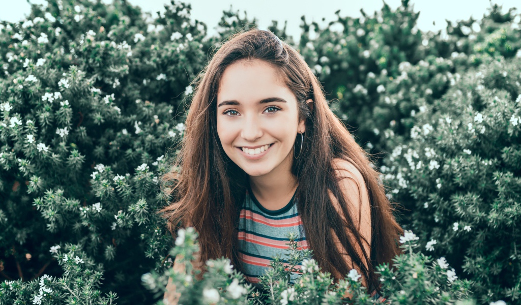 Улыбающаяся девушка сидит в зеленых зарослях 