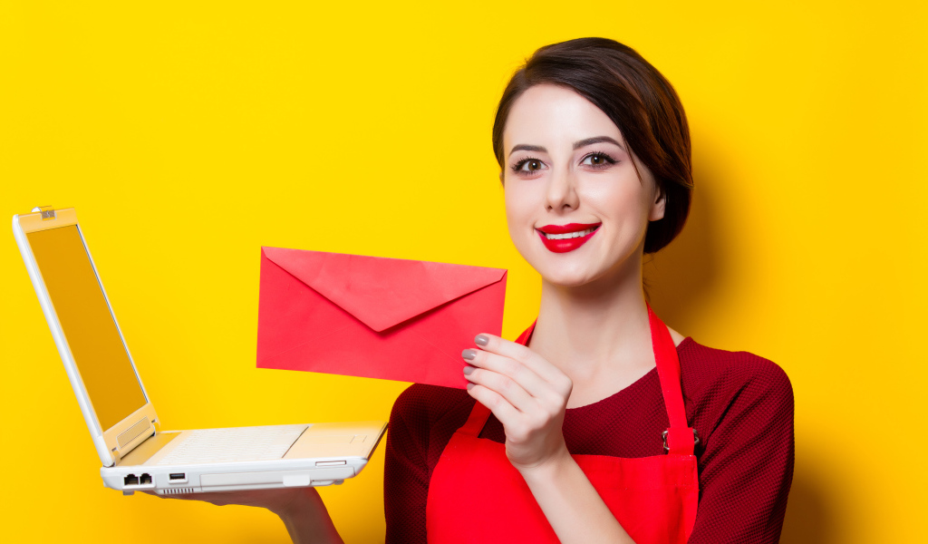 Улыбающаяся девушка с ноутбуком и конвертом в руках на желтом фоне