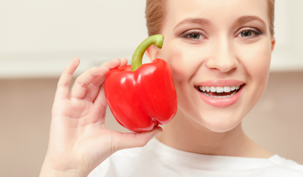 Улыбающаяся девушка с красным сладким перцем в руке