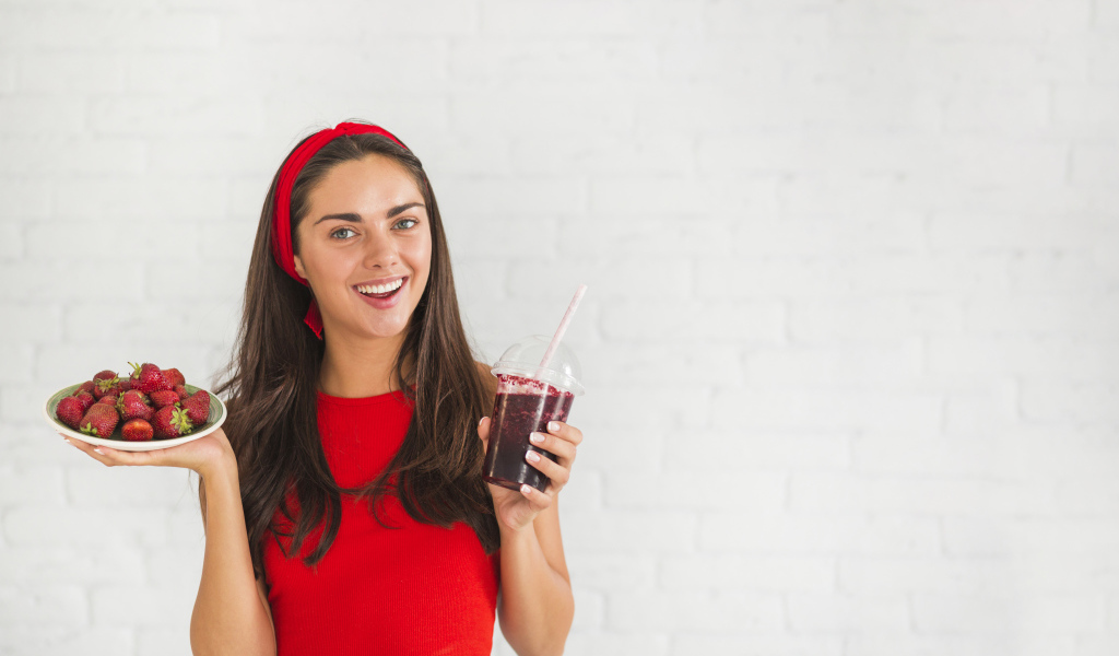 Улыбающаяся девушка с клубникой и смузи в руках