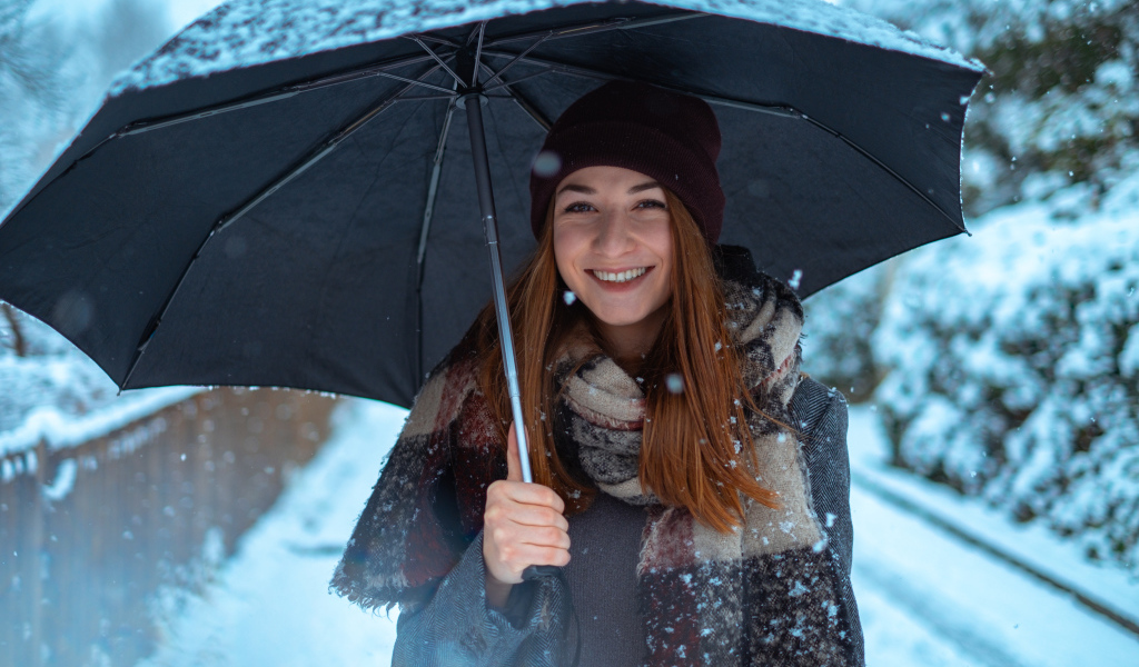 Улыбающаяся молодая девушка под зонтом зимой