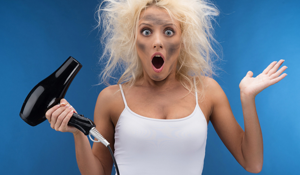 Удивленная девушка с грязным лицом с феном в руке 
