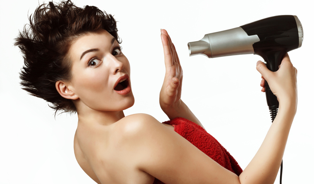 Удивленная девушка с феном в руках на белом фоне