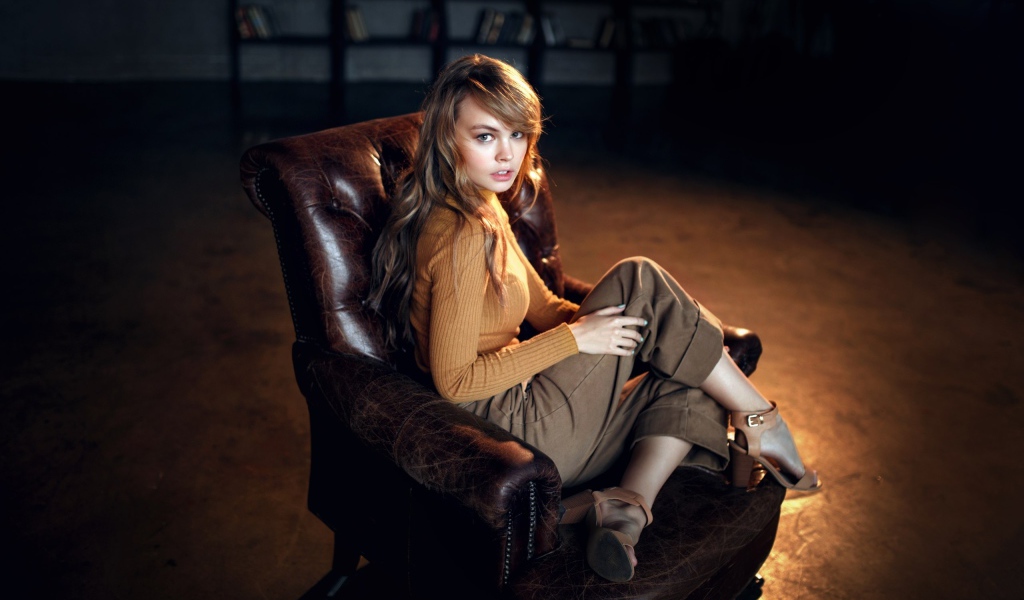 Нежная девушка модель сидит в кожаном кресле