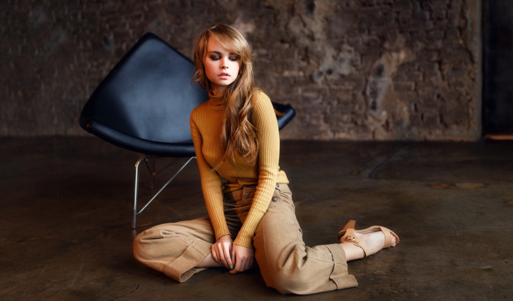 Девушка сидит на полу около черного кресла 