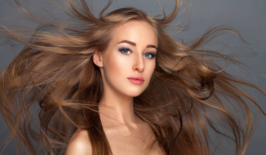Ветер развивает волосы красивой девушке на сером фоне