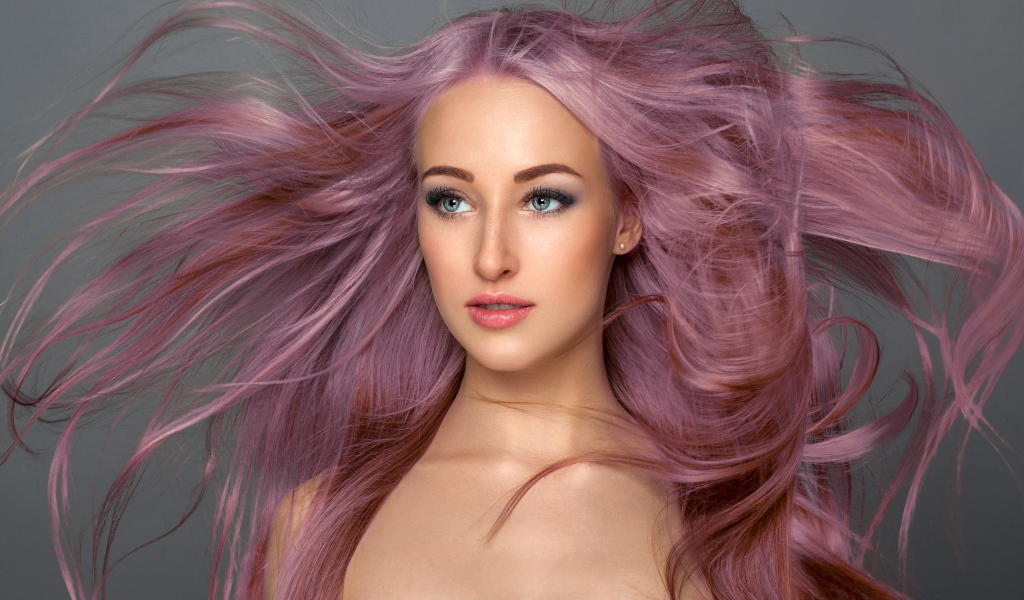 Ветер развивает розовые волосы девушки на сером фоне