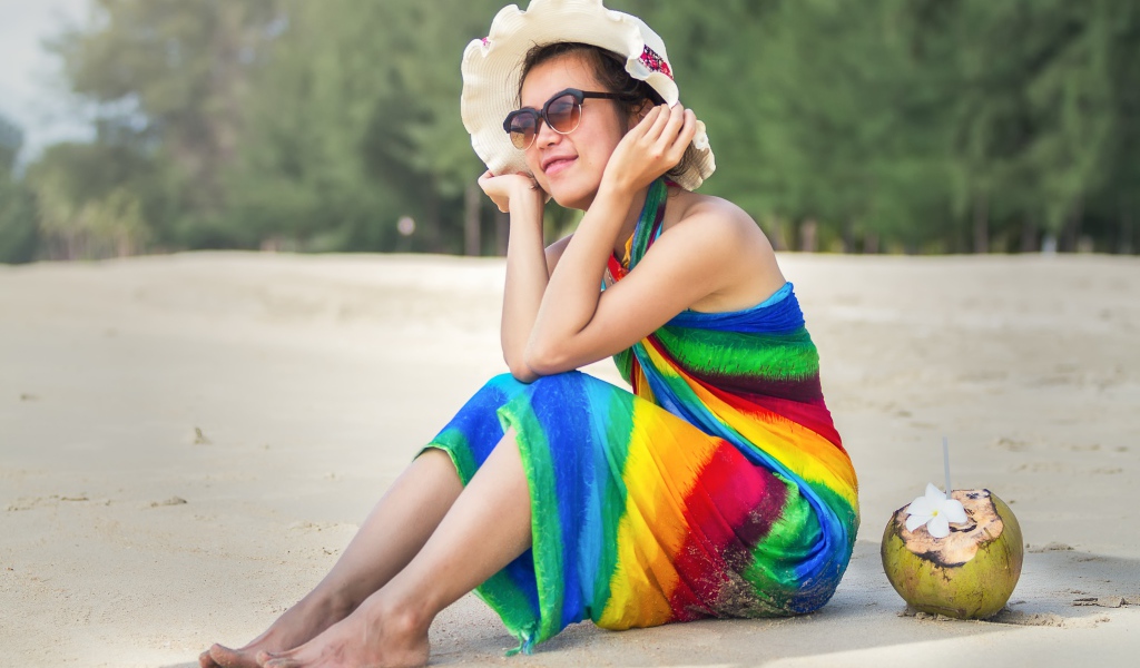 Молодая азиатка сидит на берегу с кокосом