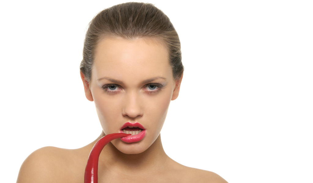 Молодая девушка кусает красный перец на белом фоне