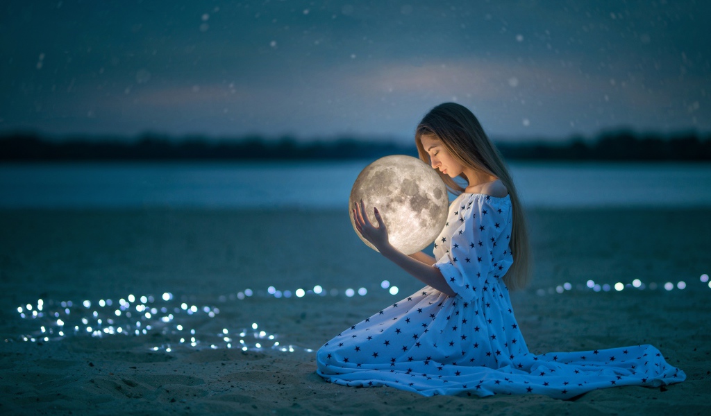 Молодая девушка в красивом платье с луной в руках на песке