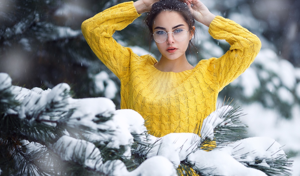 Молодая девушка в очках у заснеженной еловой ветки