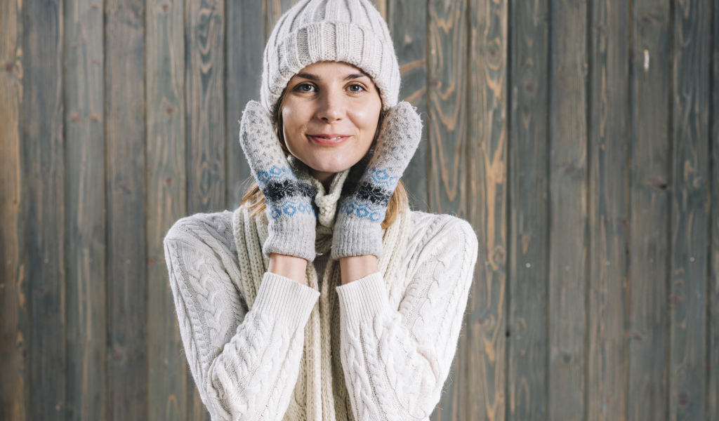 Молодая девушка на шапке, варежках  и теплой шапке на фоне забора
